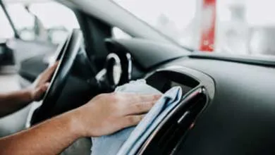Hand wiping car dashboard with blue cloth.