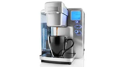 Silver, single-serve coffee maker with a blue-lit screen dispenses coffee into a black mug.