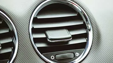 Close-up of a circular car air vent with chrome trim on a textured dashboard.