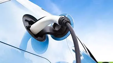 White EV charger connected to a light blue car outdoors.