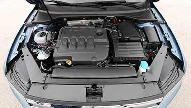 High-angle view of a light blue car's engine bay, featuring a black plastic engine cover.