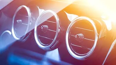 Three chrome-trimmed circular air vents on a car dashboard, illuminated by a warm sun flare from the top right.