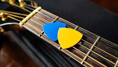Close-up of blue and yellow guitar picks resting on the fretboard of an acoustic guitar.