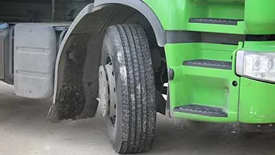 Close-up of a bright green truck’s front wheel and built-in steps.