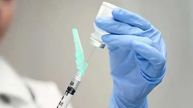 Gloved hands fill a syringe from a small vial.
