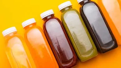 Clear plastic bottles with white caps, each filled with different colored juices, arranged diagonally on a bright yellow background.