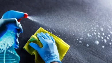 Gloved hands spraying cleaner and wiping a surface with a yellow cloth.