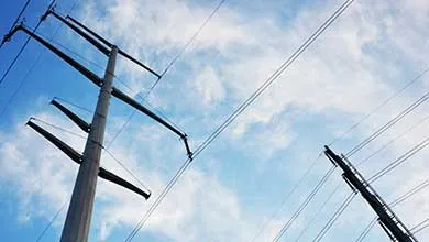 Utility poles with overhead power lines extending across a blue sky with scattered clouds.