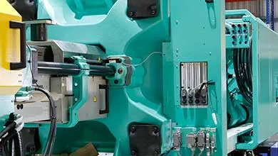 Close-up of a large teal industrial machine showing detailed mechanical parts, pistons, and hydraulic hoses.