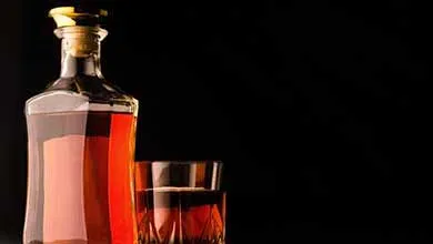 A glass decanter and a short, cut-glass tumbler filled with amber liquor are set against a black background.