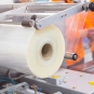 Close-up of a large roll of clear plastic film being fed into an industrial packaging machine.